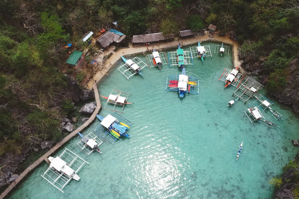 Traditional outrigger boats at the dock at Kayangan Lake, Coron, Palawan, backed by green limestone cliffs.